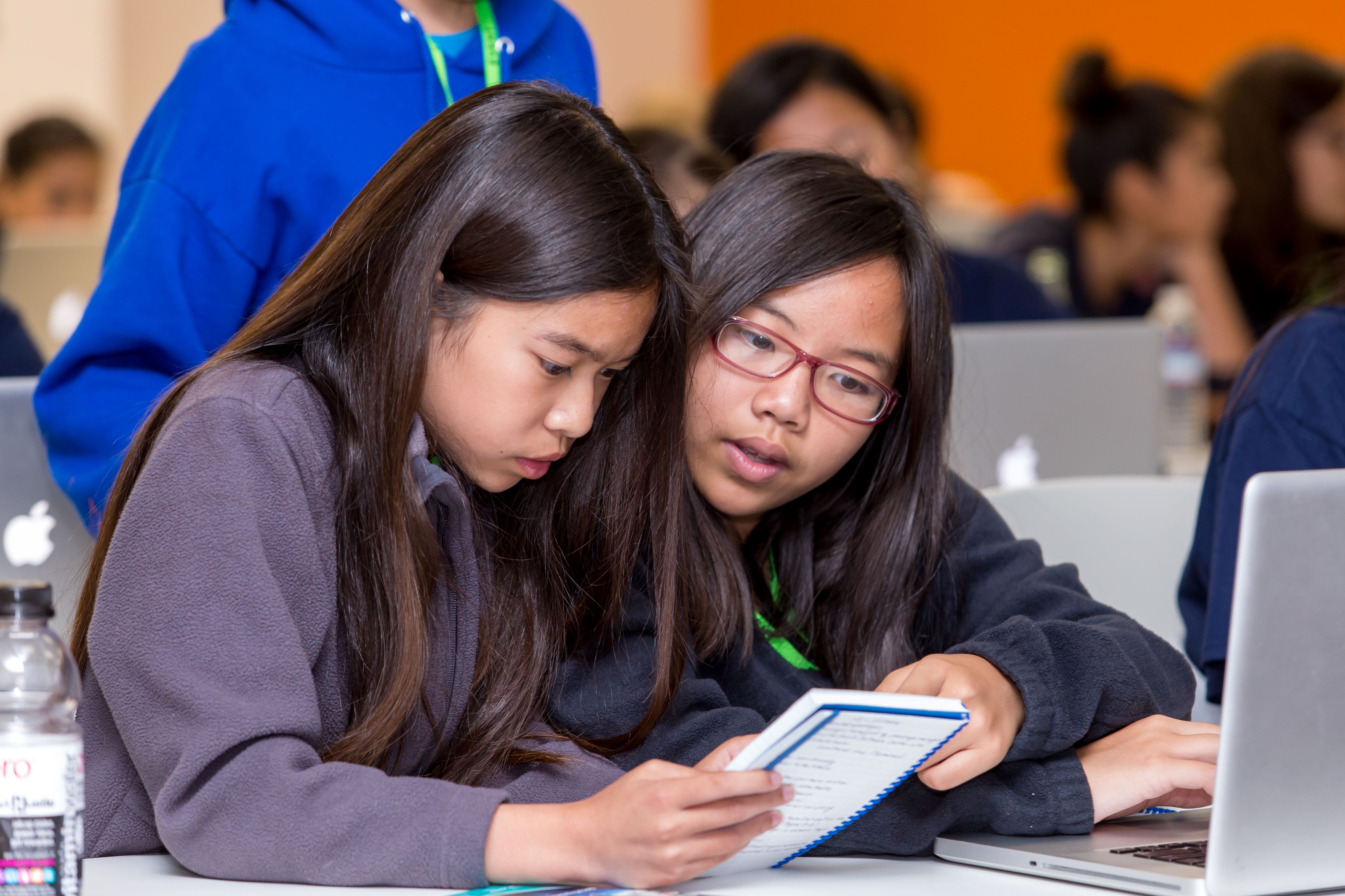 Two students sitting at a table reading a notebook