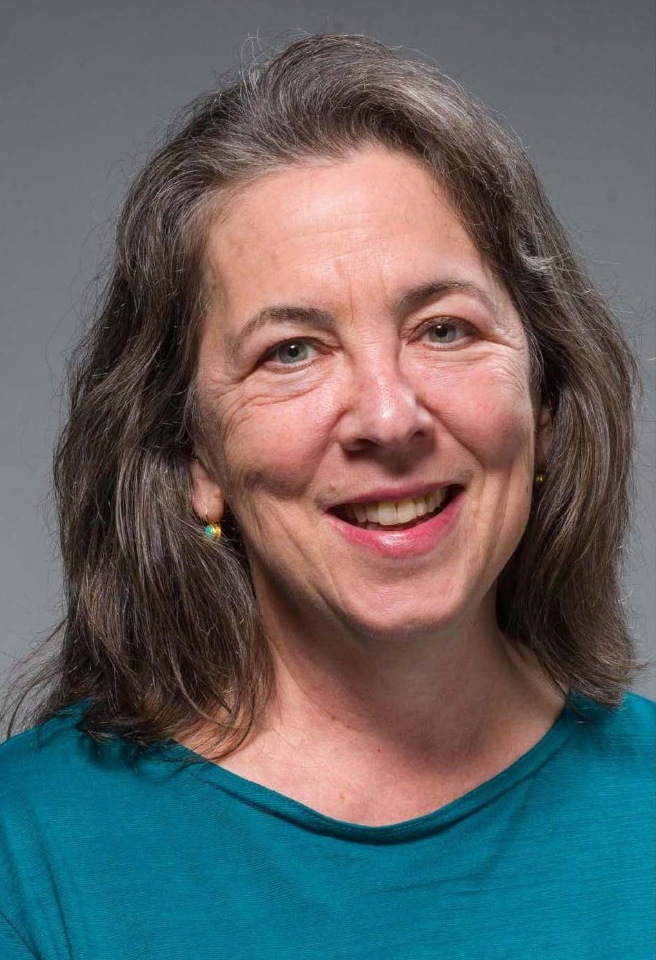 peggy-stevenson white female attorney with long, brown hair, dressed in a blue dress-shirt, smiling in front of a gray background