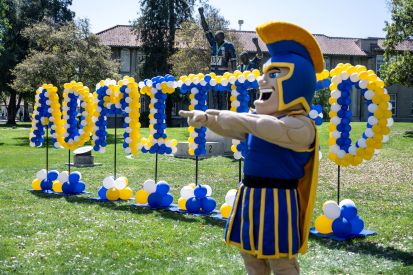 Sammy the Spartan (mascot) standing next to balloon art that spells out "Admitted."